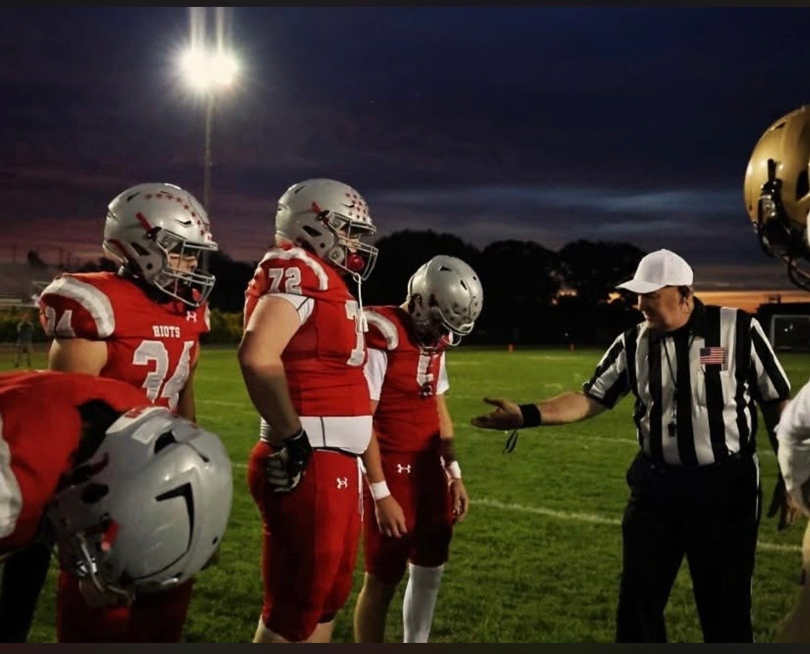 Football players in red uniforms and referees on field at night under stadium lights